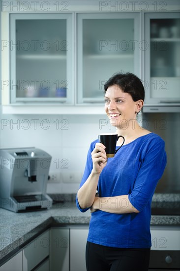 Smiling Caucasian woman drinking coffee in kitchen