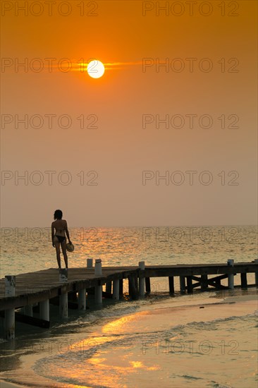 Mixed Race woman standing on ocean dock at sunset