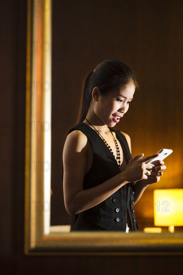 Reflection in mirror of Asian woman texting on cell phone