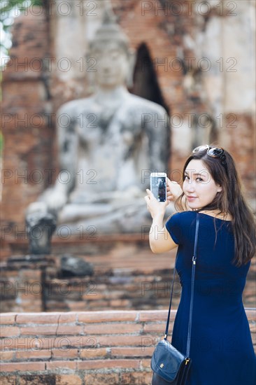 Asian woman photographing Buddha statue with cell phone