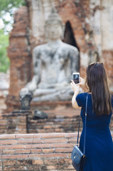 Asian woman photographing Buddha statue with cell phone