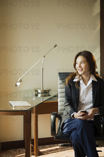 Smiling Thai businesswoman holding cell phone in office