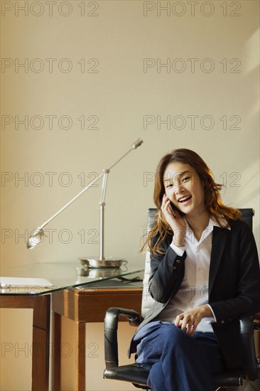 Smiling Thai businesswoman talking on cell phone in office