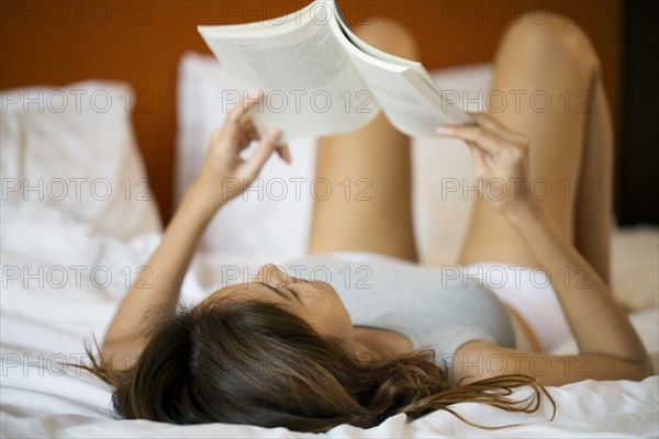 Thai woman laying in bed reading book