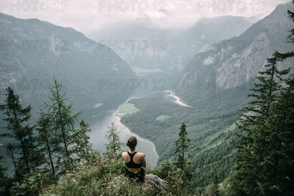 Caucasian woman sitting on rock overlooking lake in valley