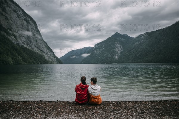 Caucasian couple sitting near mountain lake