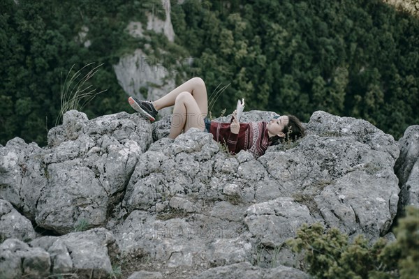 Caucasian woman laying on mountain rocks reading magazine