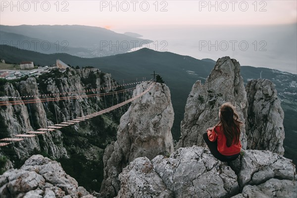 Caucasian woman sitting on mountain near footbridge