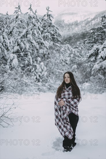 Caucasian woman wrapped in blanket in snowy forest