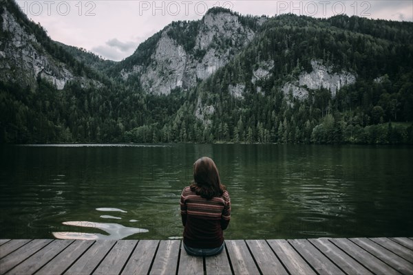 Caucasian woman sitting on dock admiring scenic view of mountain