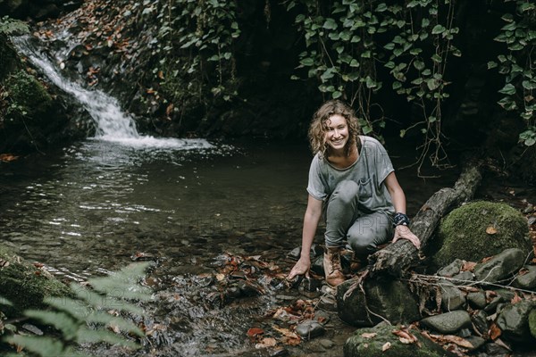 Caucasian woman crouching on rock in forest stream