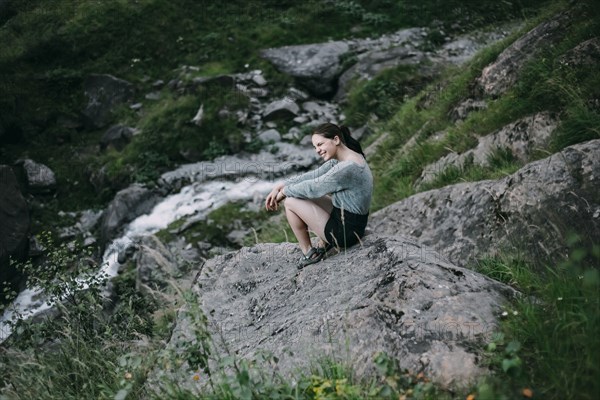 Smiling Caucasian woman sitting on rock on hill