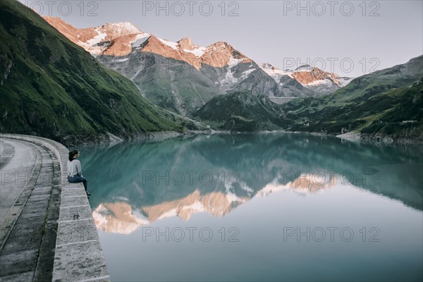 Caucasian woman sitting on wall at mountain lake