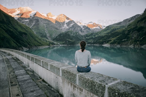 Caucasian woman sitting on wall at mountain lake