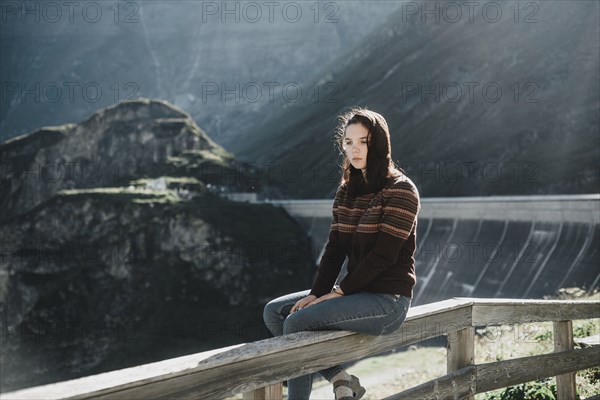 Pensive Caucasian woman sitting on wooden fence
