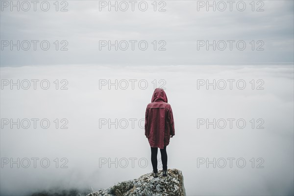 Distant Caucasian woman standing on rock watching fog on ocean