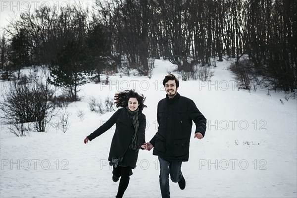 Caucasian couple running from forest in winter