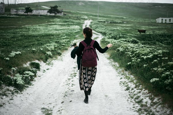 Caucasian woman walking on dirt road carrying wildflowers