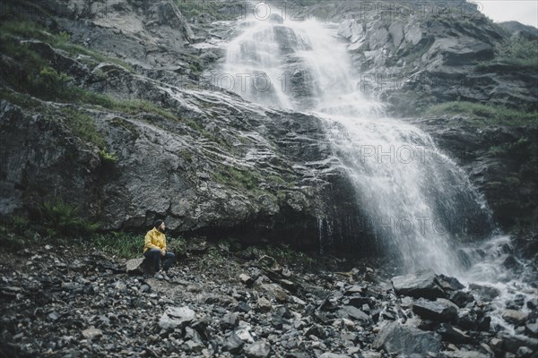 Caucasian man sitting on rock watching waterfall