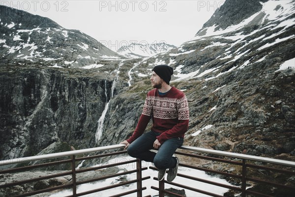 Caucasian man sitting on balcony railing admiring snow on mountain