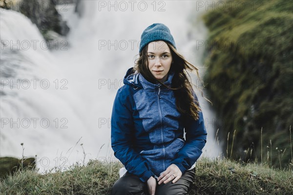 Portrait of serious Caucasian woman sitting near waterfall
