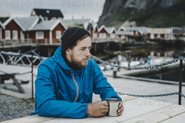 Pensive Caucasian man drinking coffee at table at waterfront