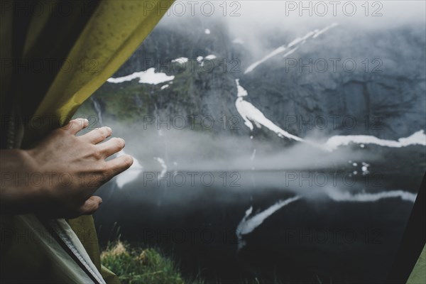 Hand opening tent flap near foggy river