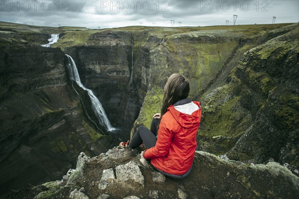 Caucasian woman sitting on cliff admiring waterfall