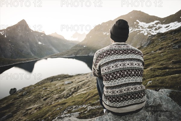 Caucasian man sitting on rock admiring scenic view of mountain lake