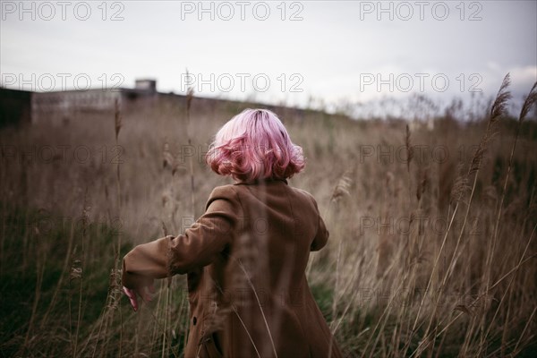 Caucasian woman with pink hair running in field