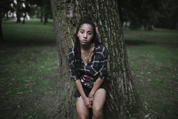 Portrait of serious African American woman leaning on tree