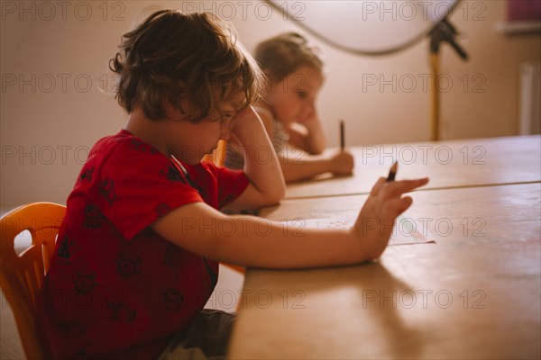 Caucasian boy and girl sitting at table with pencil and paper