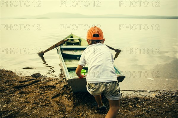 Caucasian boy pushing boat into still lake