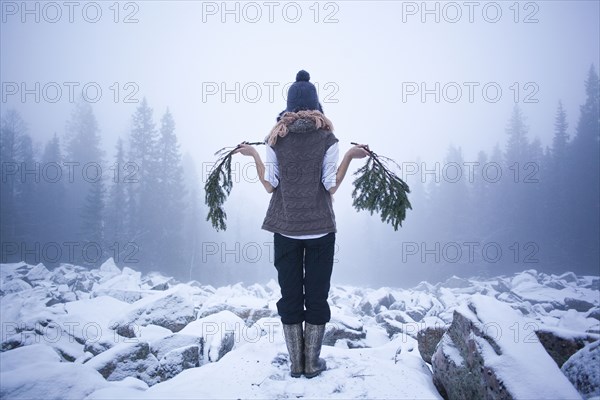 Caucasian woman holding tree branches on snow covered rocks