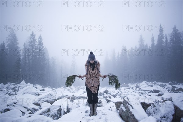 Caucasian woman holding tree branches on snow covered rocks