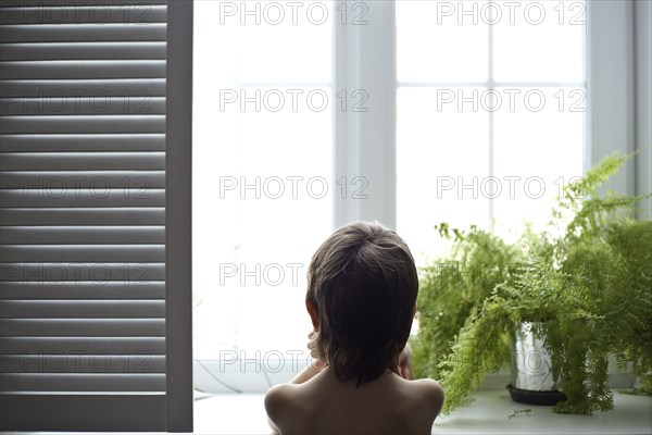 Asian boy looking out bedroom window