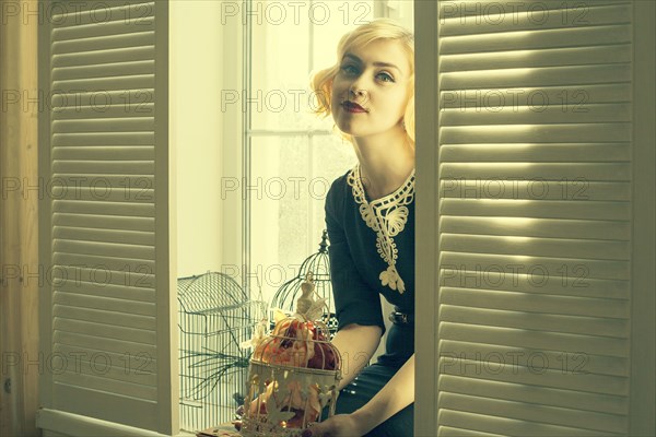 Caucasian woman holding birdcage in window