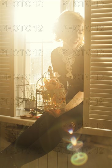 Caucasian woman holding birdcage in window