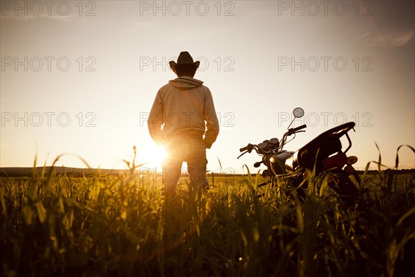 Mari man standing in field with motorcycle