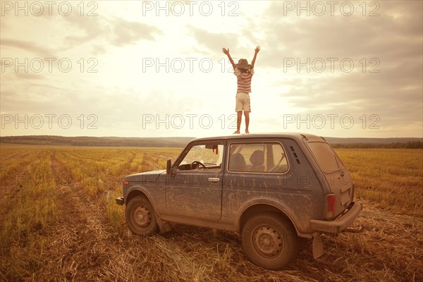 Mari boy standing on car roof in rural field