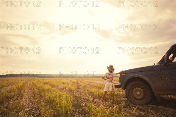 Mari boy leaning on car in rural field