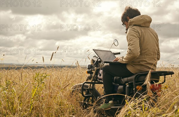 Mari man using laptop on motorcycle in rural field