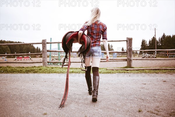 Caucasian woman carrying horse saddle on ranch