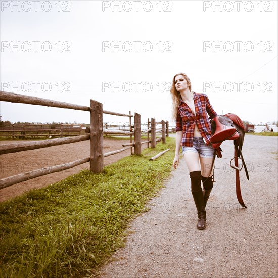 Caucasian woman carrying horse saddle on ranch