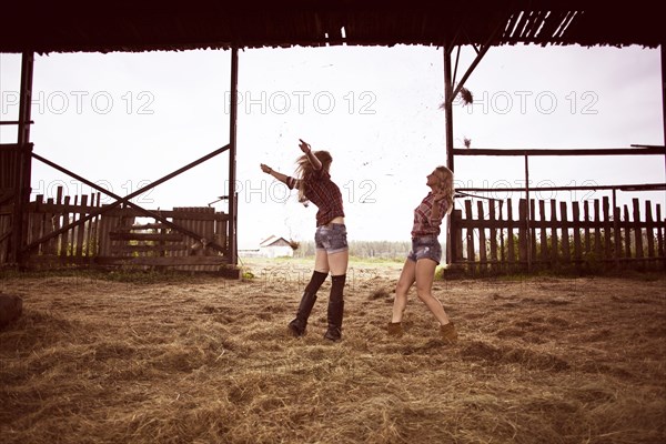 Caucasian women playing in hay in barn