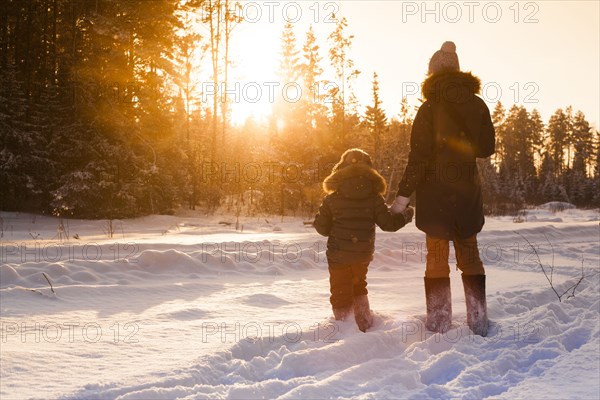 Mother and son walking in snowy forest clearing