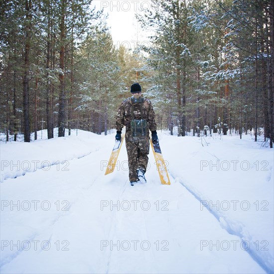 Caucasian man carrying skis on snowy road