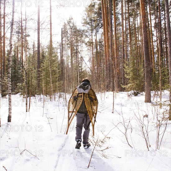 Mari man carrying snowshoes in snowy forest