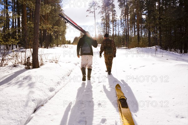 Men carrying skis on snowy path