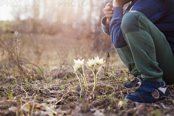 Mari boy crouching near flowers in forest